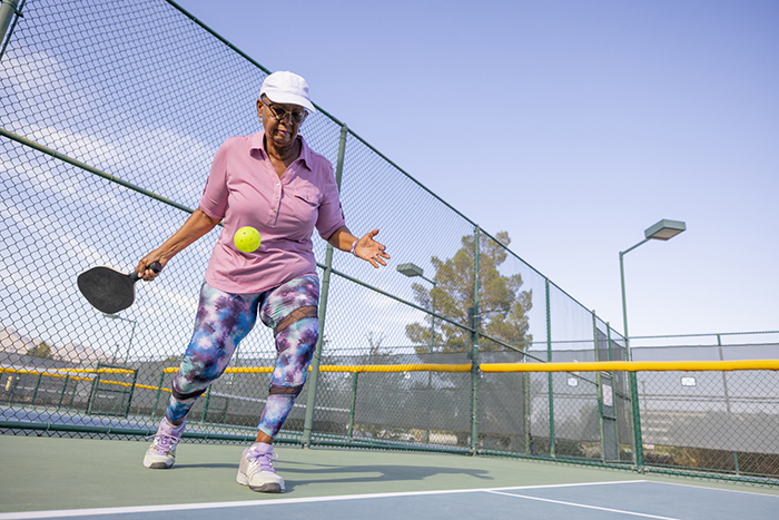 Mujer con camiseta rosa jugando al pickleball en una pista de tenis