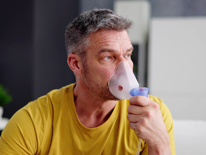un hombre con camisa amarilla utiliza una mascarilla de oxígeno y un nebulizador para la COPD