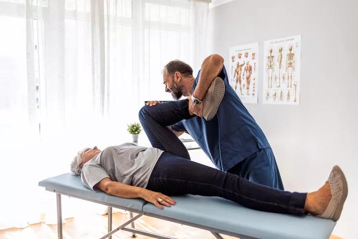 Male doctor chiropractor or osteopath fixing womans leg with hands movements during visit in manual therapy clinic